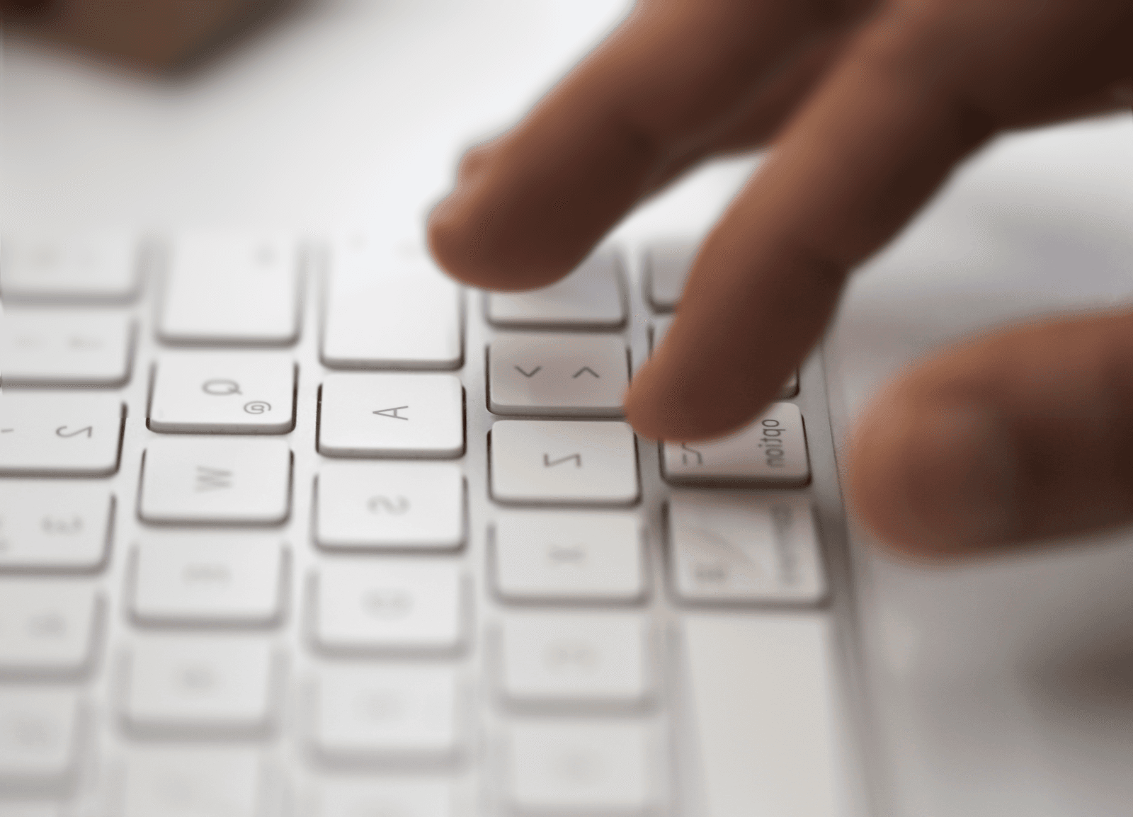 Close-up of fingers typing on a white keyboard, focusing on the arrow keys and surrounding letters.