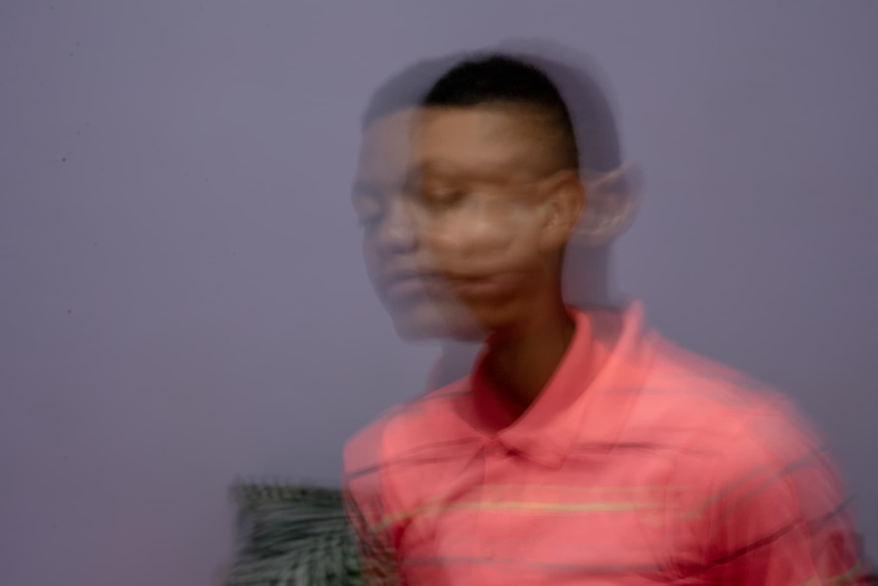 A person in a pink shirt appears with a blurred, double exposure effect against a plain background.