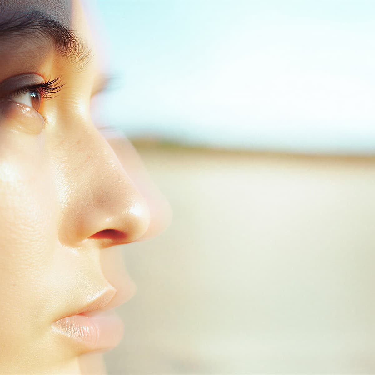 Close-up side profile of a person's face against a blurred background, highlighting smooth skin and eye gazing ahead.