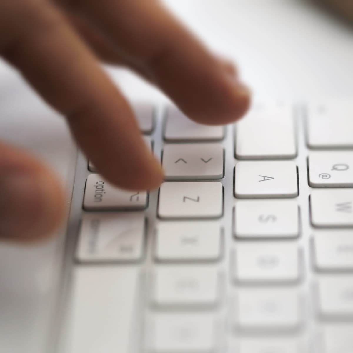 A hand typing on a white keyboard, focusing on the "Z" and "Option" keys with blurred fingertips for emphasis.