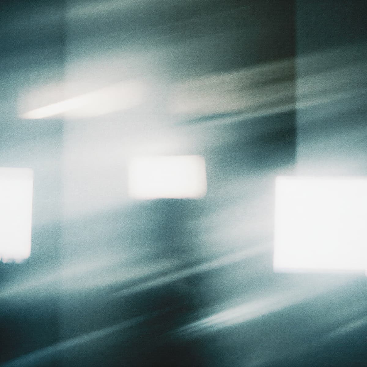 Abstract image of blurred light streaks and squares on a dark background, creating a sense of motion and ethereal atmosphere.