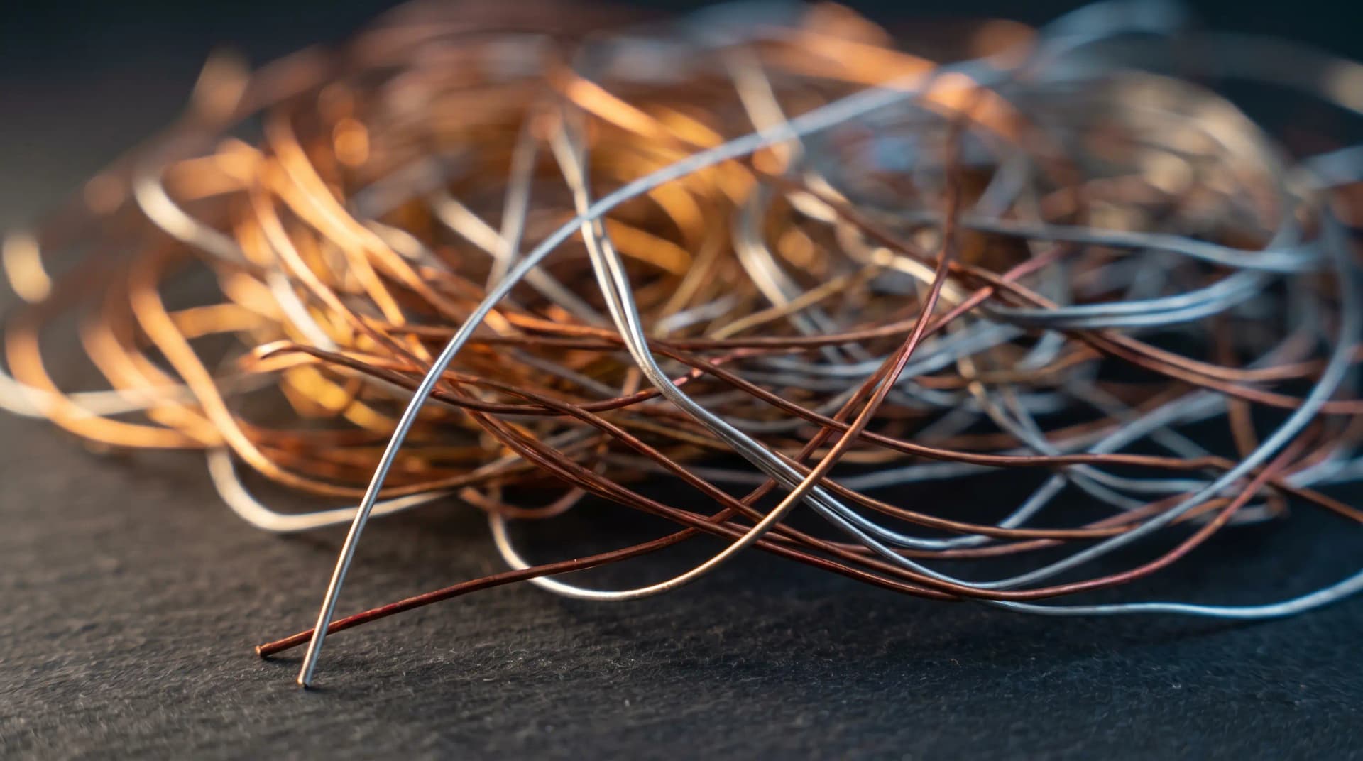 Close-up of tangled copper and silver wires on a dark background, showcasing their metallic textures and colors.