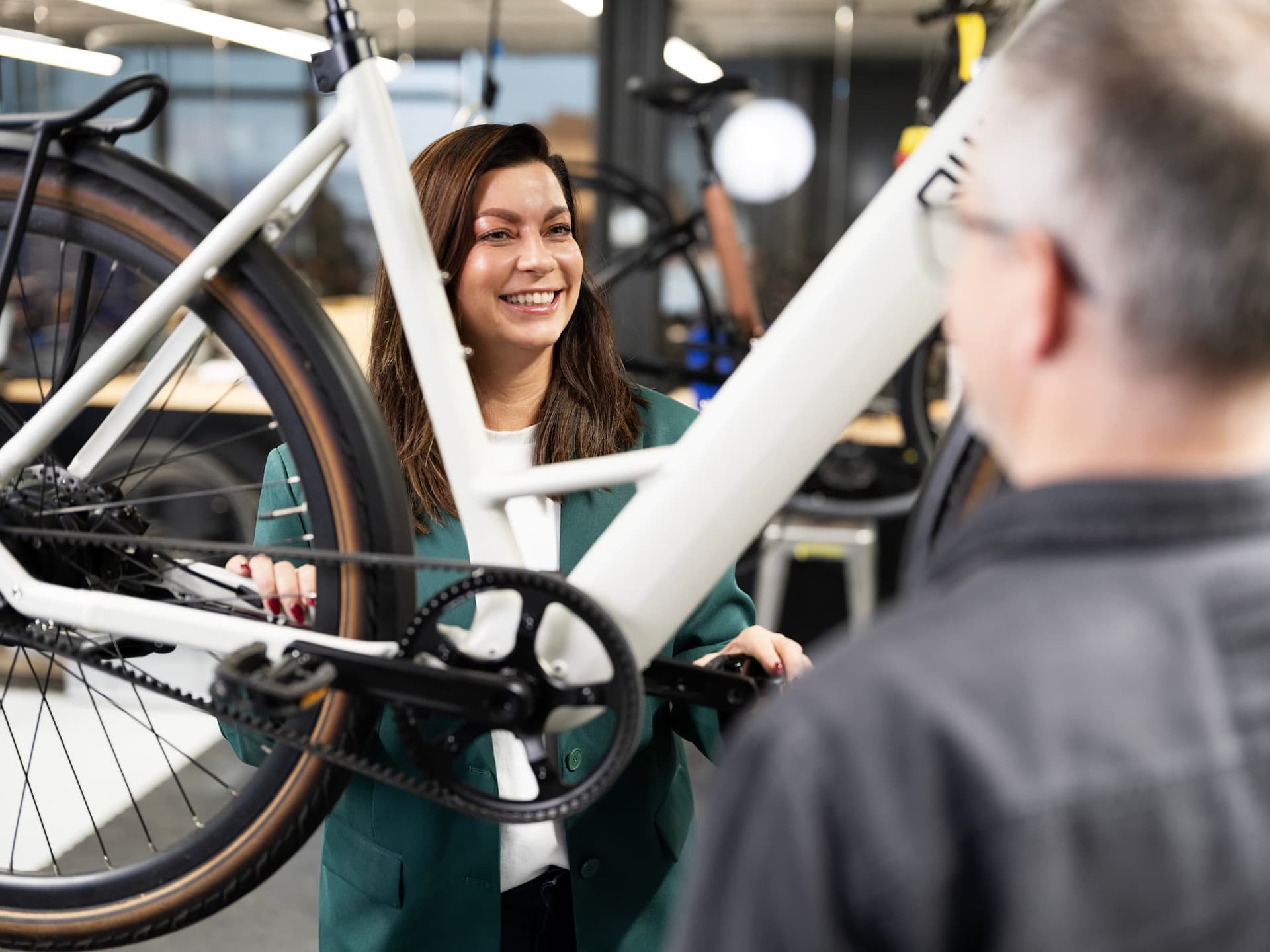 A woman and a man in a workshop examine a white bicycle. The woman smiles while they discuss the bike's features.
