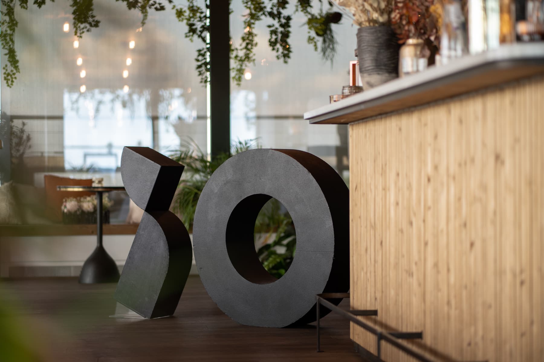 Large black sculptures of the letters "i" and "O" sit beside a wooden counter in a modern interior with plants and soft lighting.