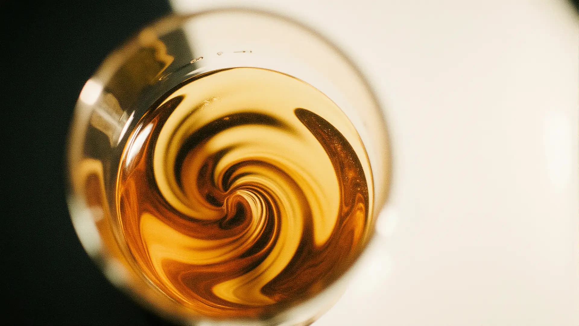 Top view of a glass of swirling brown liquid with a vibrant, dynamic spiral pattern against a softly blurred background.