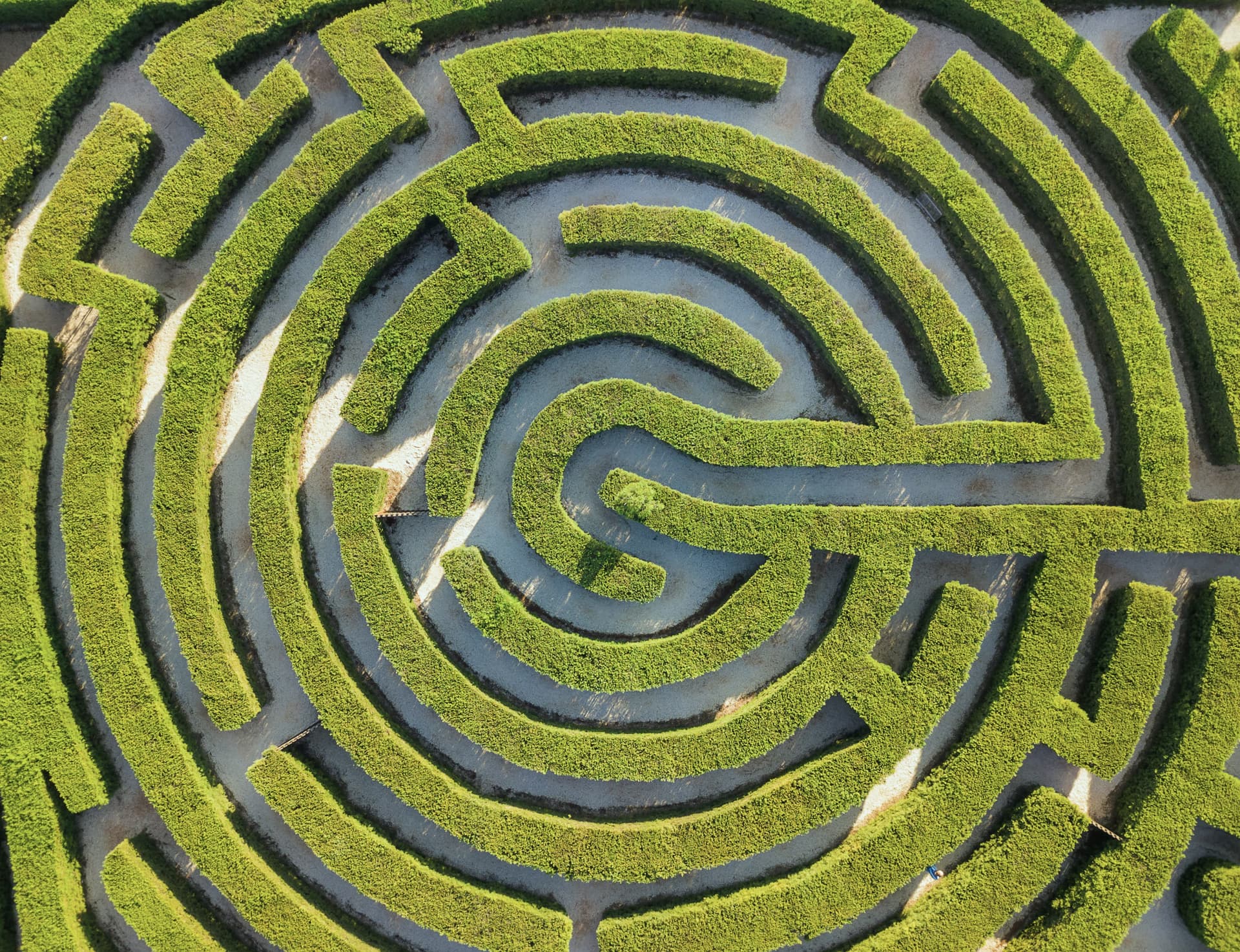 Aerial view of a circular garden maze with lush green hedges and winding paths, creating an intricate pattern.