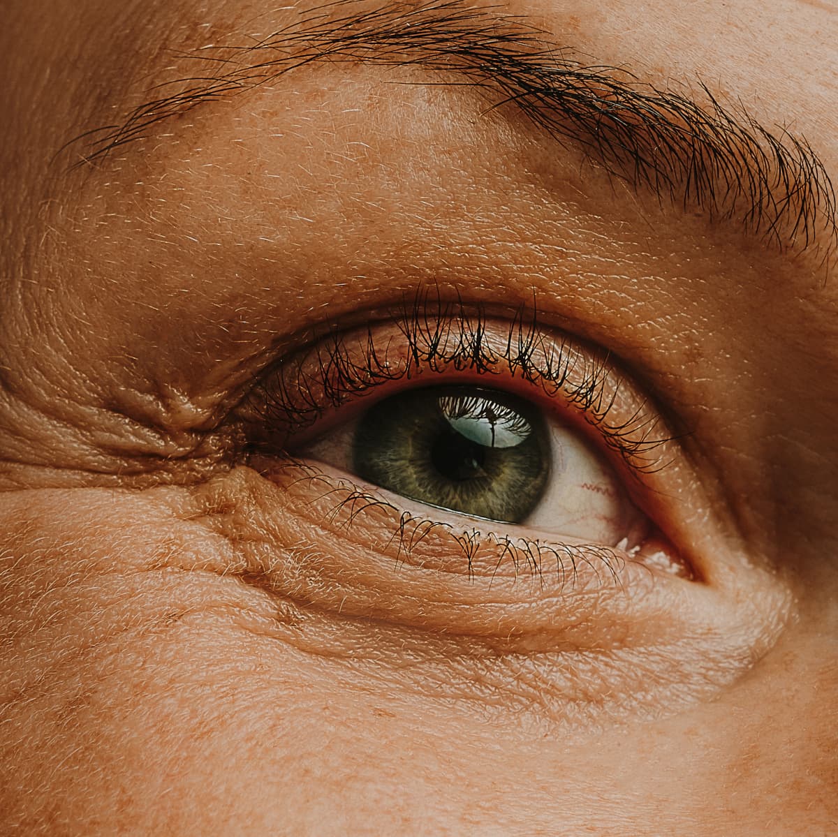 Close-up of a human eye with green iris, visible eyelashes, and detailed skin texture around the eye.