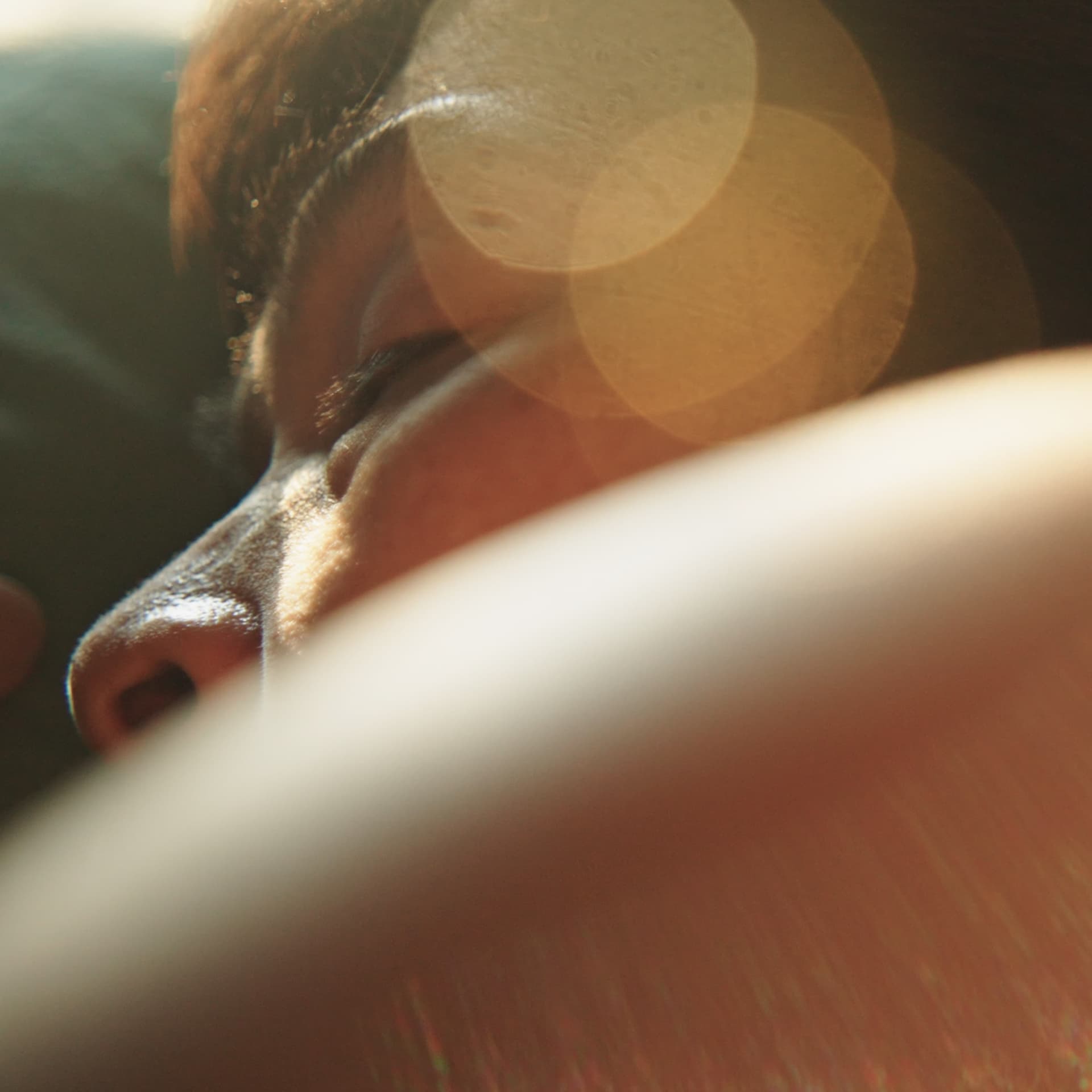 Close-up of a person's face in soft focus with warm sunlight and lens flare effects, creating a dreamy atmosphere.
