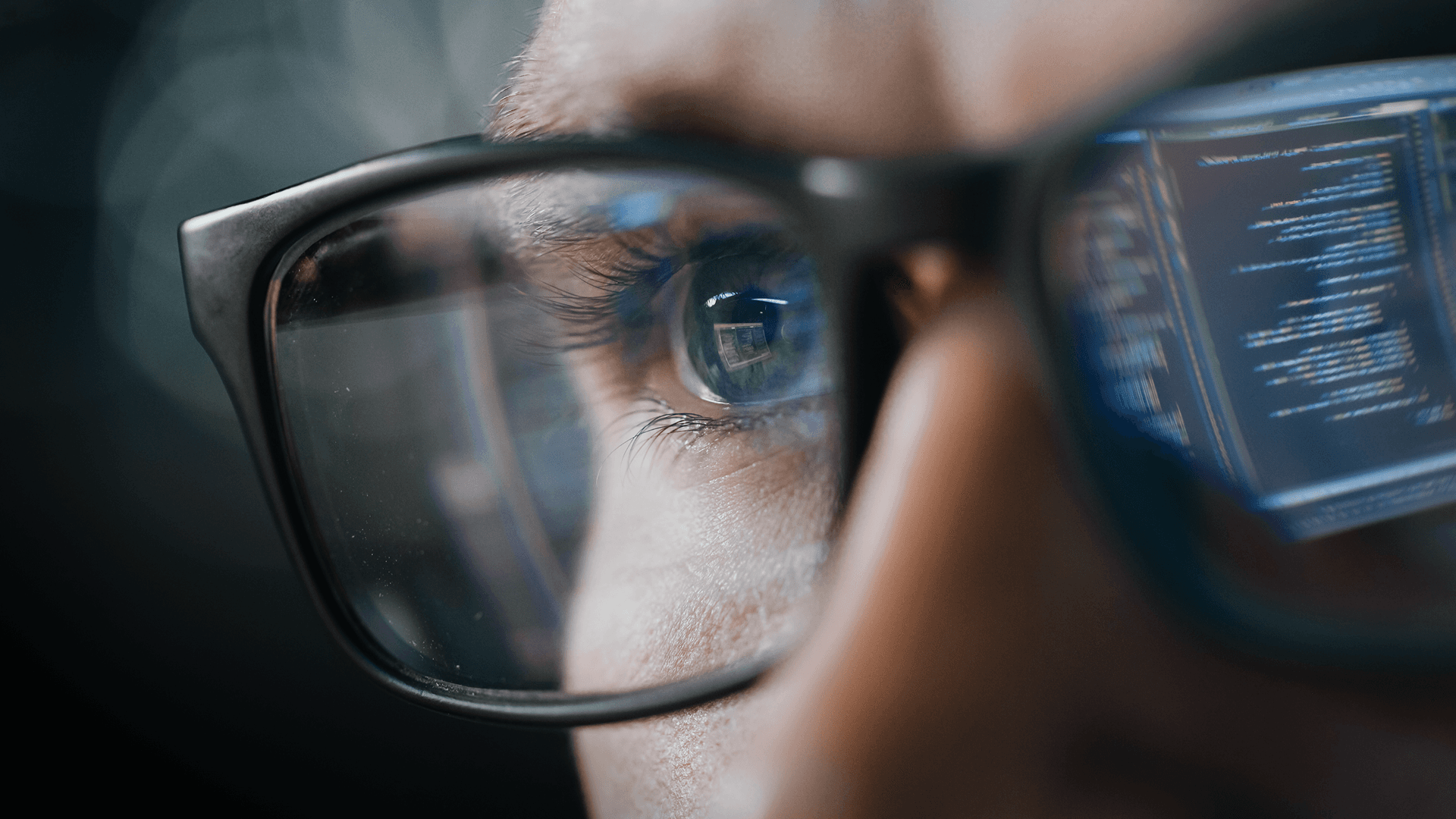 Close-up of an eye focused on coding reflected in eyeglasses, with computer code visible on the lens.