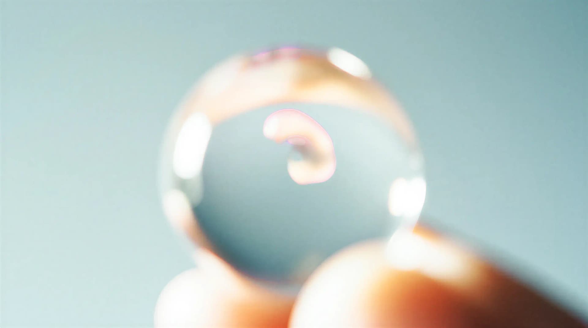 Close-up of a blurry clear contact lens on a finger, with a hint of colorful reflection, against a soft blue background.