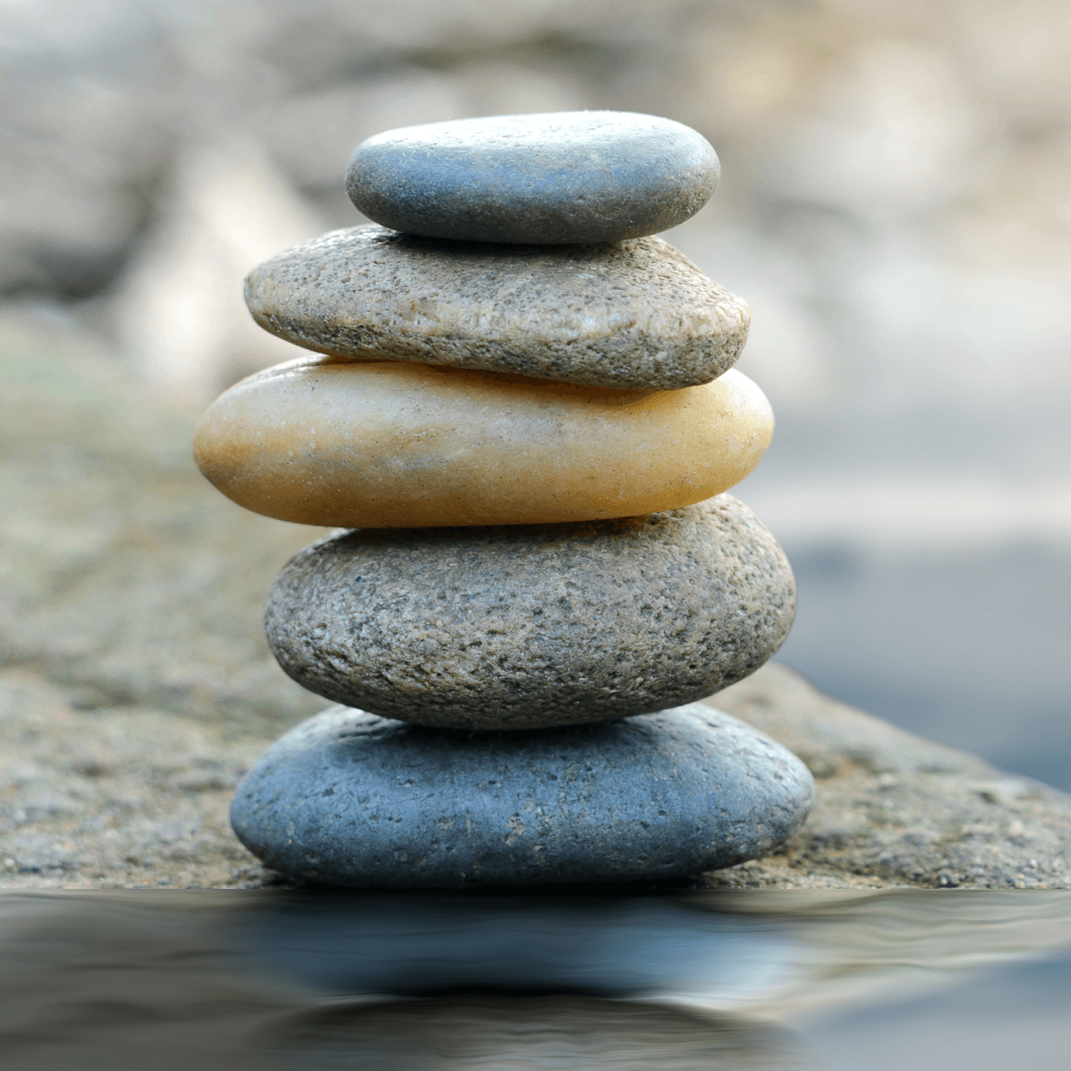 A stack of smooth, rounded stones in varying shades of gray and beige, balanced on a rock with a blurred natural background.