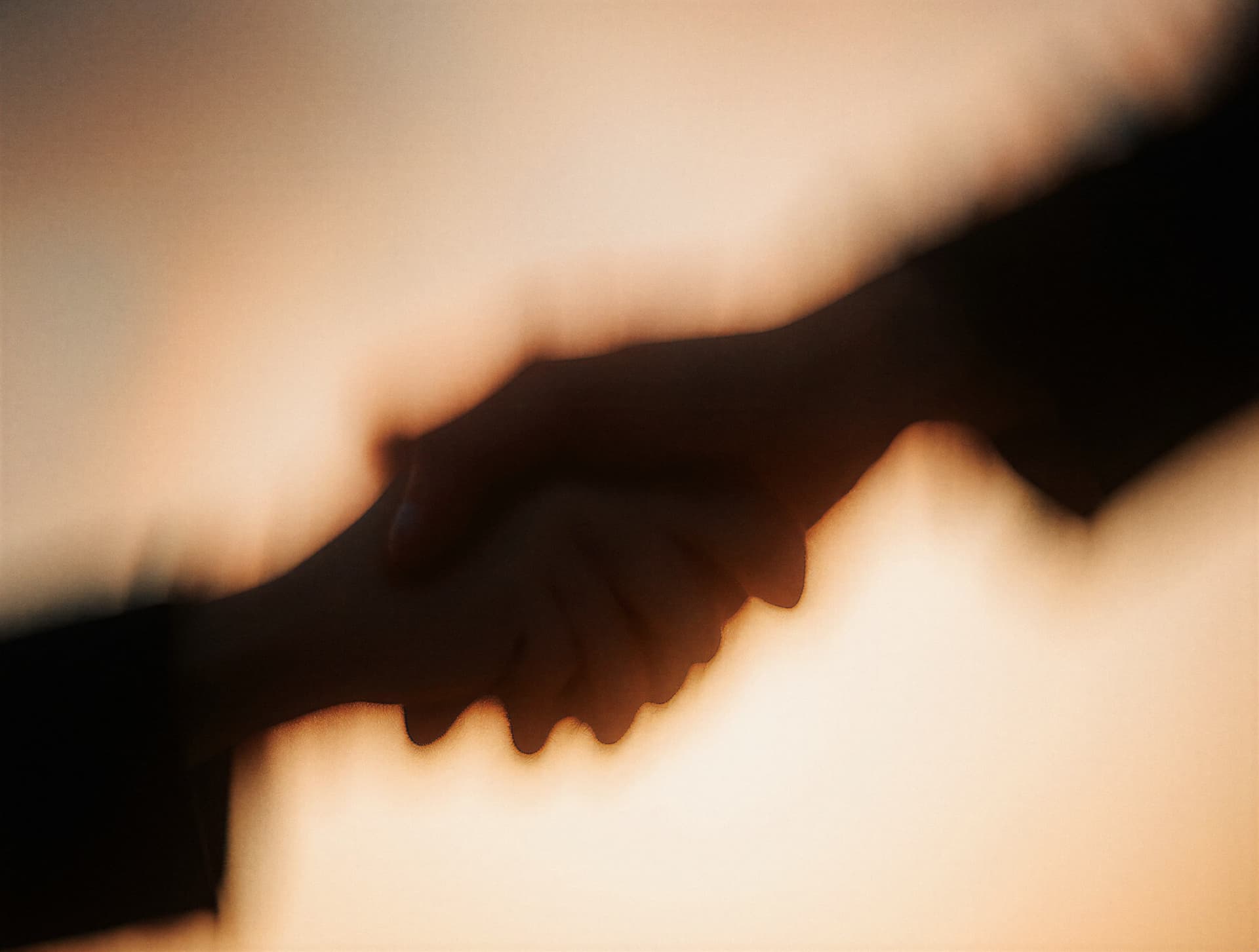 Silhouetted handshake with blurred motion effect against a warm sunset background.