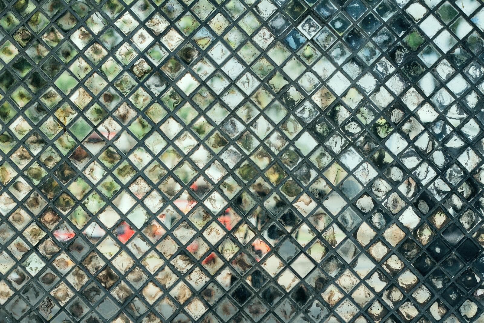 Patterned glass surface with small diamond shapes, obscuring a view of outdoor greenery and blurred colors behind.