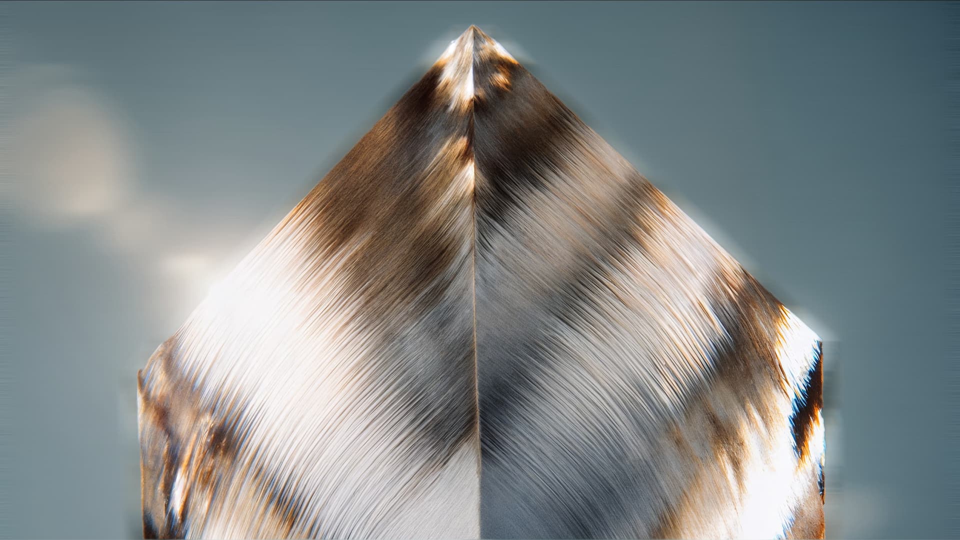 Close-up of a shiny, angular crystal sculpture with textured brown and silver surfaces against a blurred gray background.