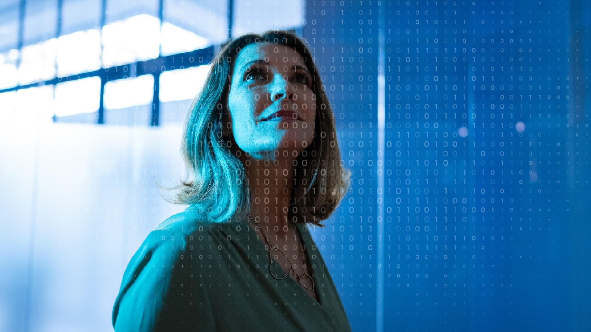 Woman in a blue-lit room looks up thoughtfully, with binary code overlaying the image, suggesting technology and innovation themes.