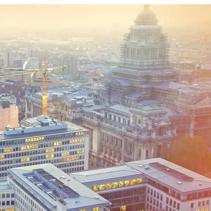 Aerial view of an ornate historic building surrounded by modern office buildings at sunset, with a construction crane visible in the background.