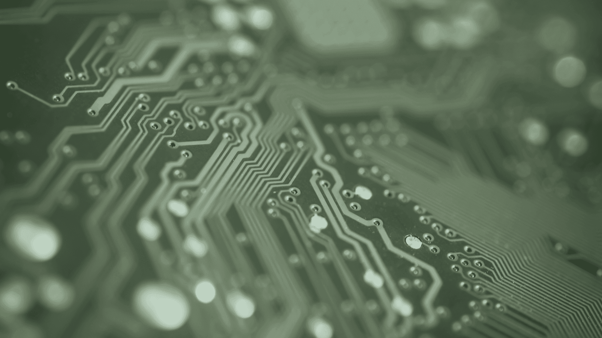 Close-up of a green printed circuit board with intricate silver lines and various connections.