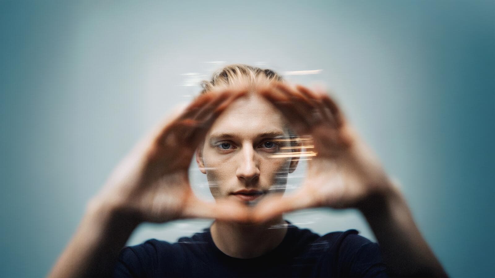 Person looking through hands forming a circle, with motion blur effect, against a blurred blue background.