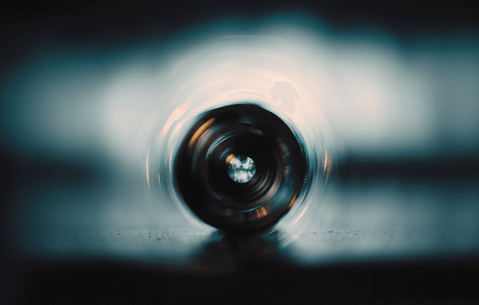 Blurred close-up of a camera lens on a reflective surface, surrounded by soft, swirling glow with blue and orange hues.