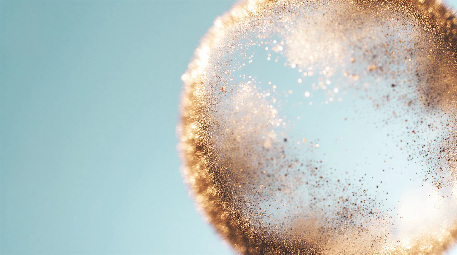 Close-up of golden dust particles floating in the air against a soft blue background, creating an ethereal, shimmering effect.