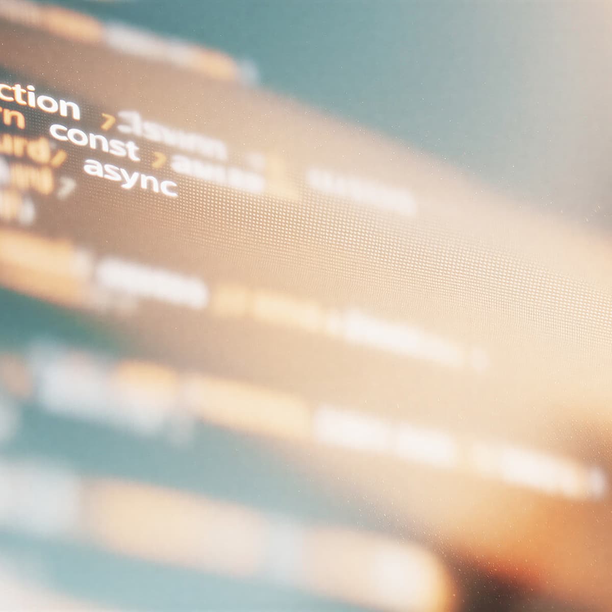 Blurry close-up of a computer screen displaying lines of code with terms like "function," "const," and "async," in warm light.