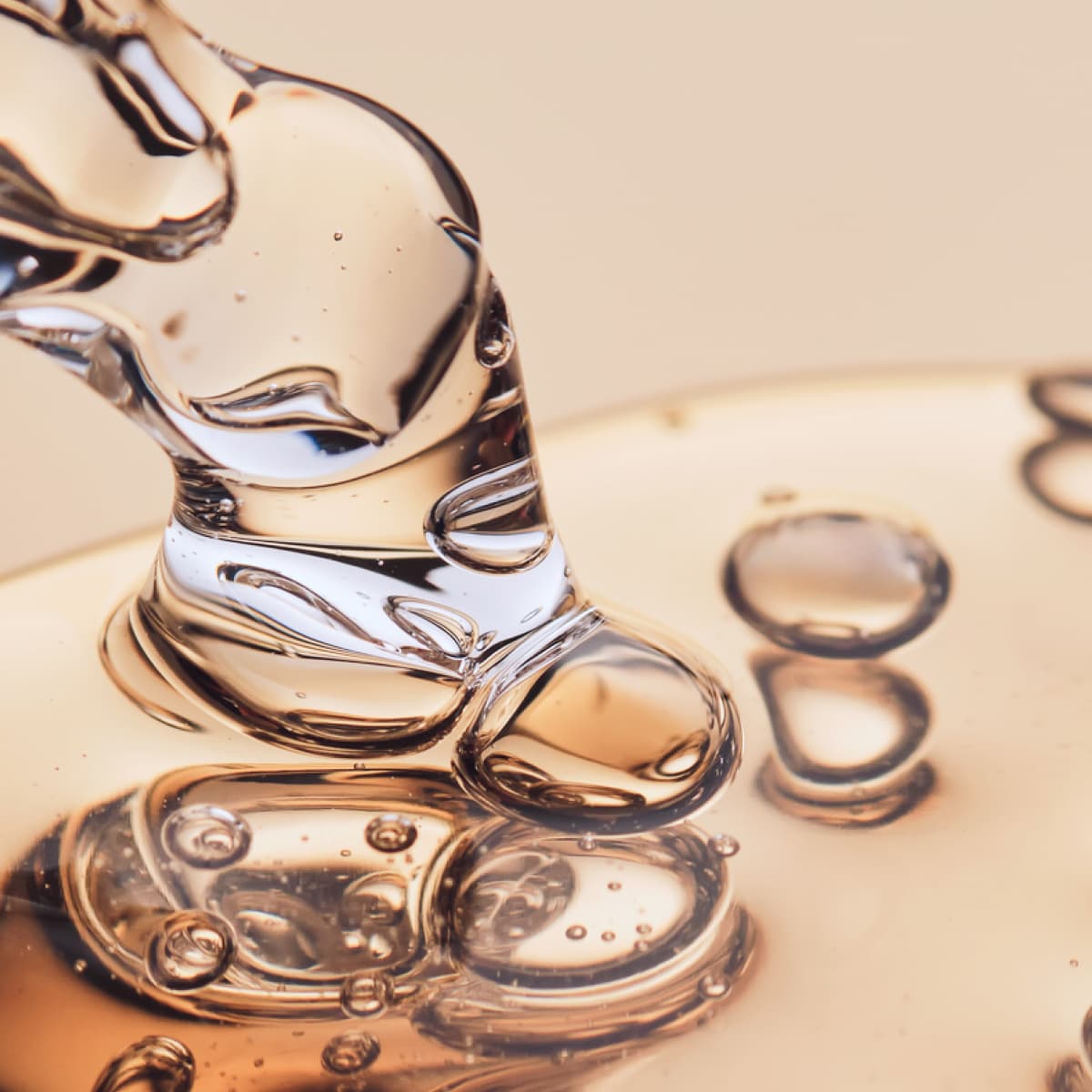 Close-up of translucent gel pouring and forming bubbles on a smooth surface, with a soft beige background.