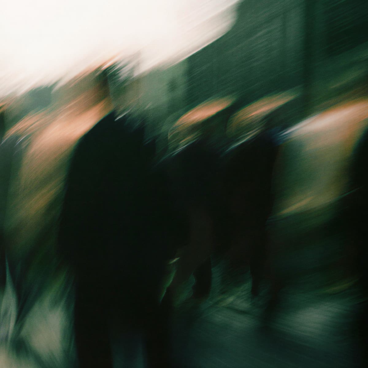 Abstract, blurry image of people moving in a cityscape, with dark green and brown tones, creating an impressionistic effect.