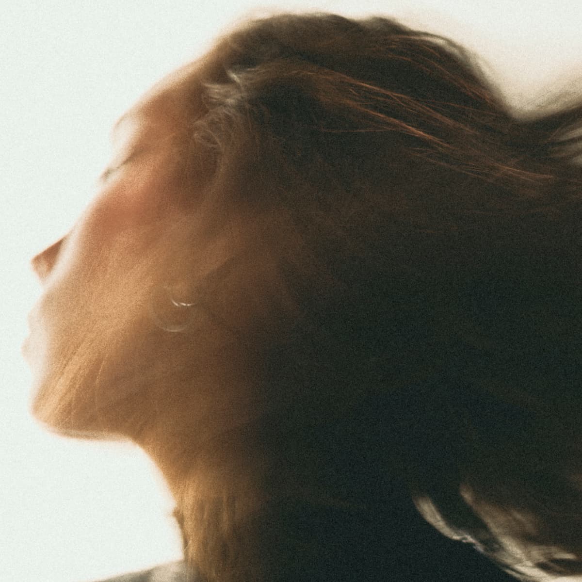 Blurry profile of a person with long hair flowing dramatically to the side, set against a light background.