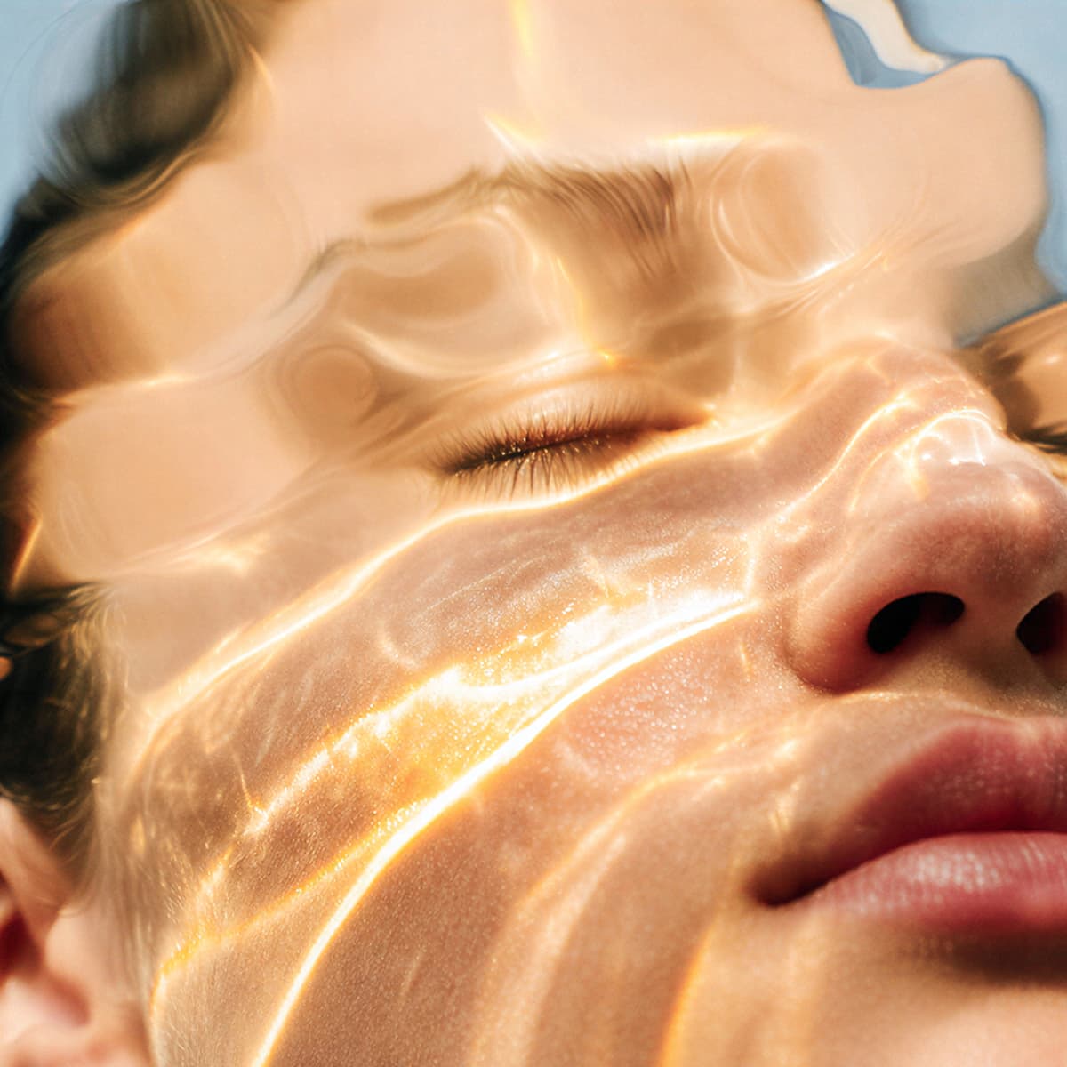 Close-up of a person's face partially submerged in water, with sunlight creating shimmering patterns on the skin.