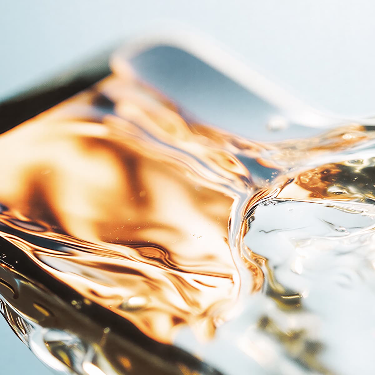 Close-up of swirling golden liquid with reflective highlights, creating a sense of motion and texture with a hint of transparency.