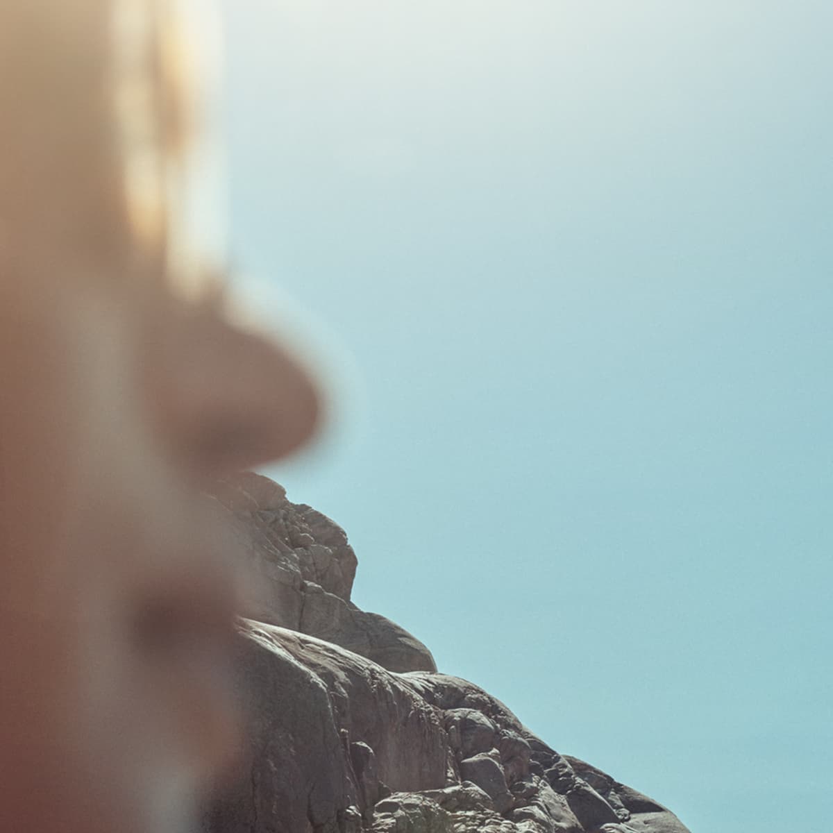 Blurred close-up of a person with glasses and a mountain under a clear blue sky.