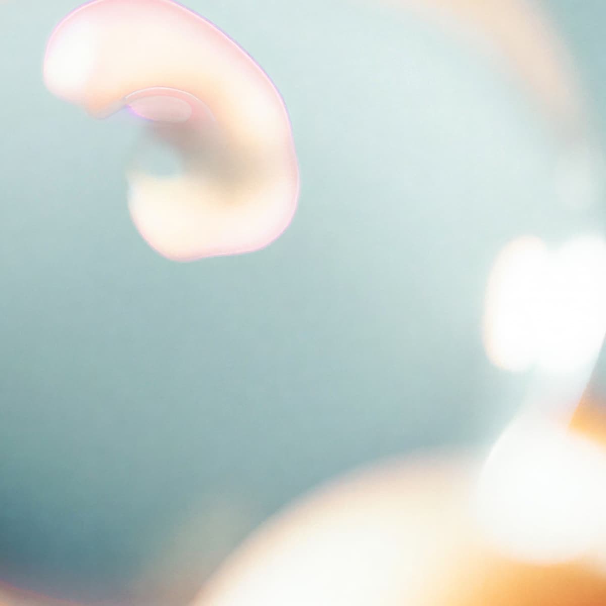 An abstract close-up of a light pink and beige swirl against a soft blue and white background, creating a dreamy, ethereal effect.
