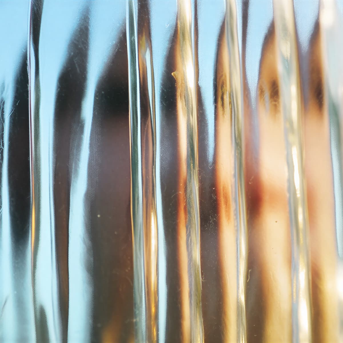 Abstract image with vertical ripples in glass, creating a blurred effect with a mix of blue, orange, and brown hues.