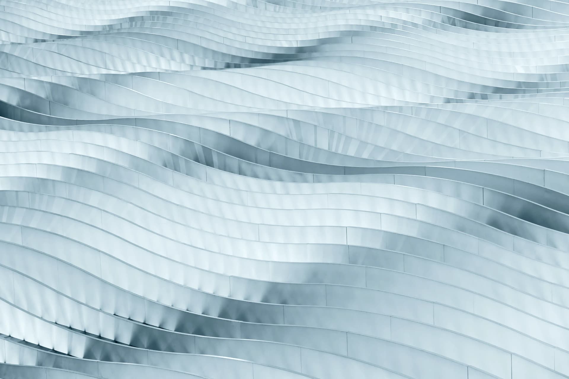 Abstract pattern of wavy, metallic-like surfaces with a smooth, flowing texture in shades of light blue and gray.