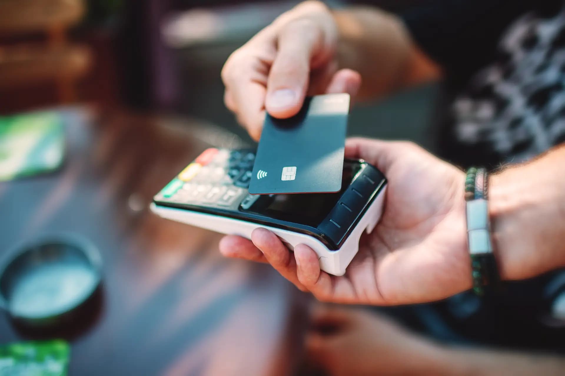A person holds a credit card near a payment terminal for a contactless transaction.