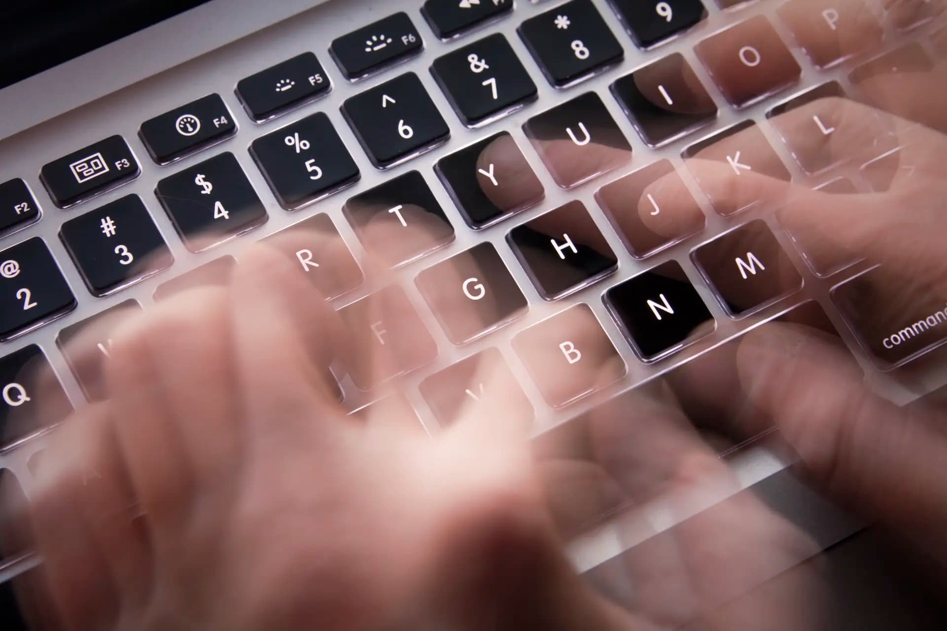 Blurry hands typing quickly on a laptop keyboard, capturing a sense of speed and motion.