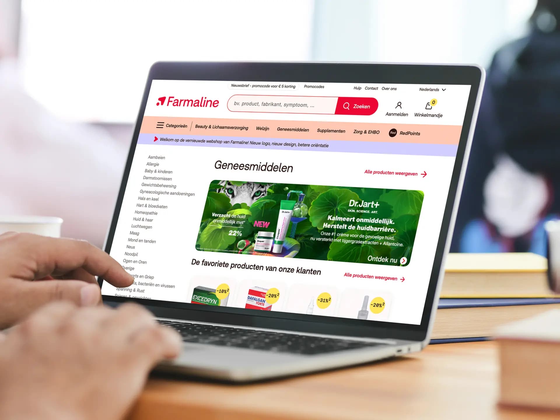 Person browsing Farmaline's pharmacy website on a laptop, showcasing Dr.Jart+ products and various health categories.