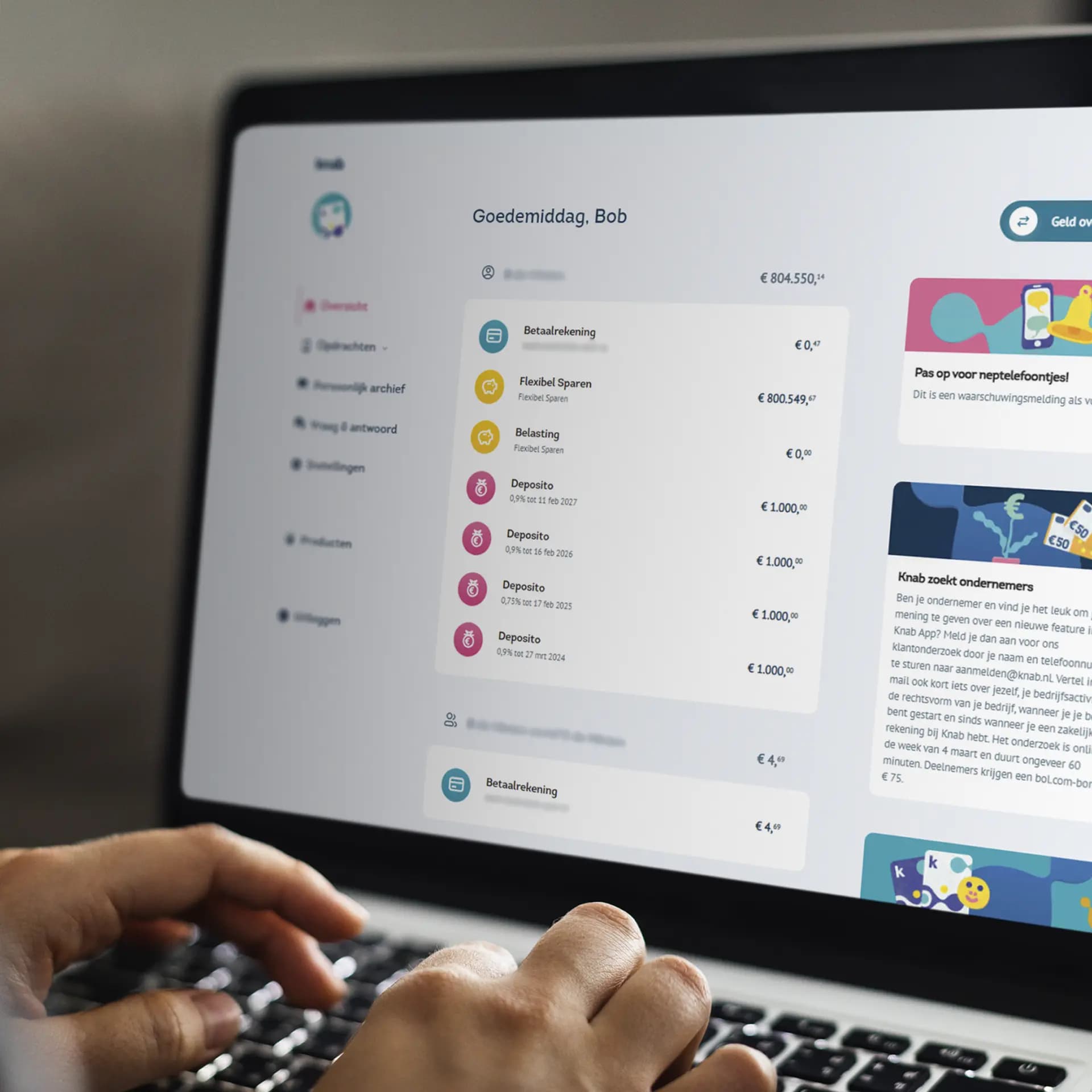A person typing on a laptop displaying an online banking dashboard with account details, savings, and deposits.