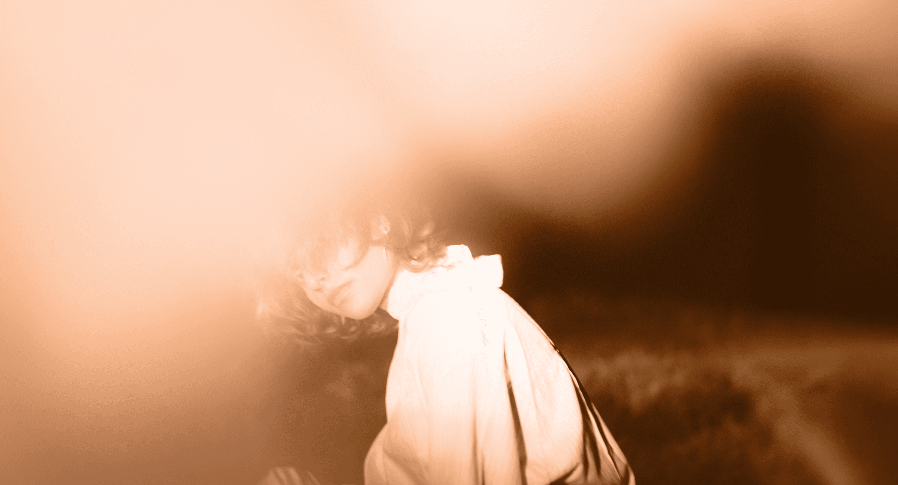 A person in a white shirt partially obscured by a soft, warm blur, creating a dreamy and ethereal atmosphere.
