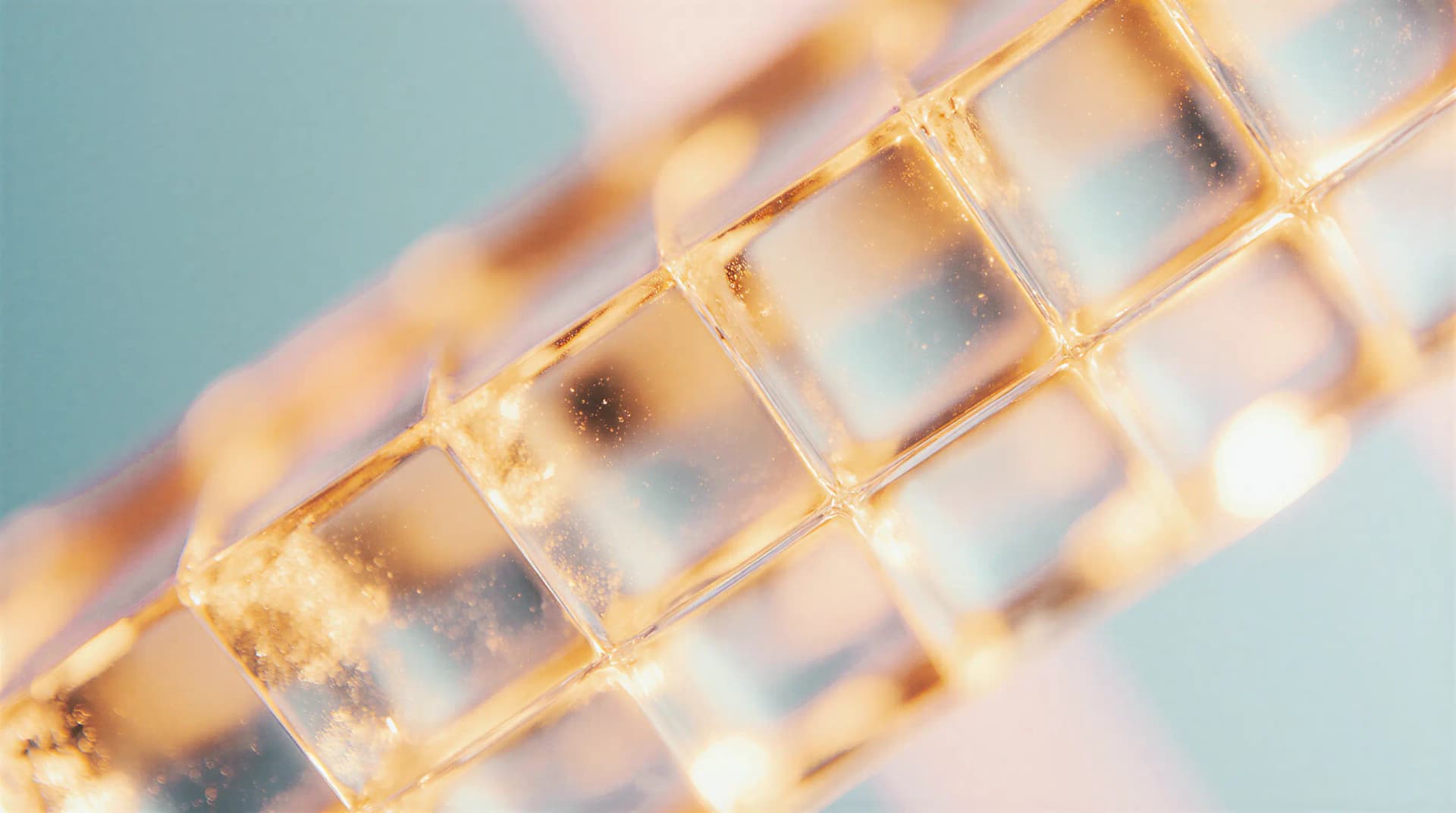 Close-up of translucent golden-tinted cubes, arranged in a diagonal line, with a shimmering and softly blurred background.