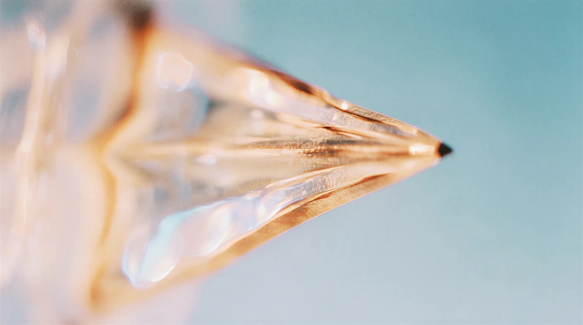 Close-up of a sharpened pencil tip with a reflective, metallic texture against a soft blue background.