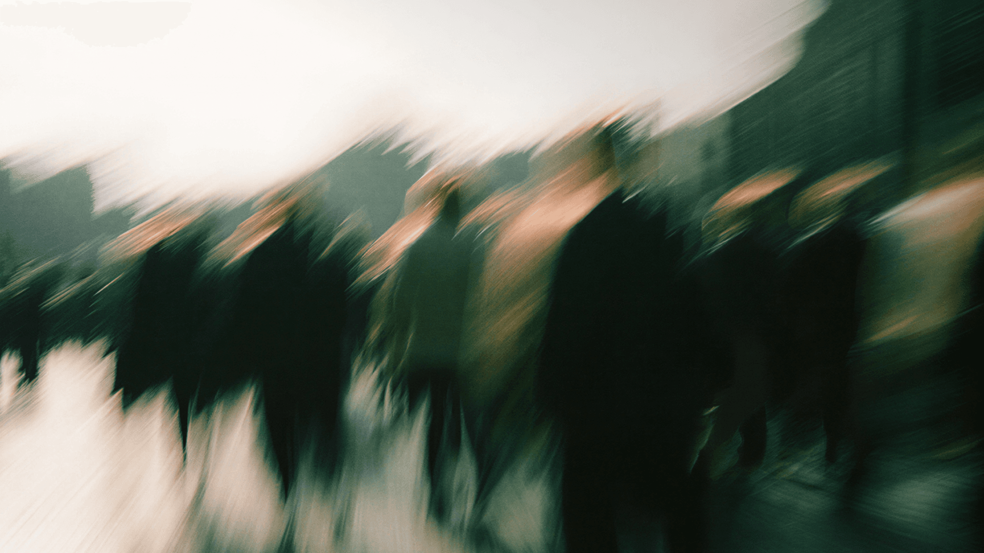 Blurred image of people walking in a cityscape, creating a dynamic abstract effect with motion and indistinct figures.