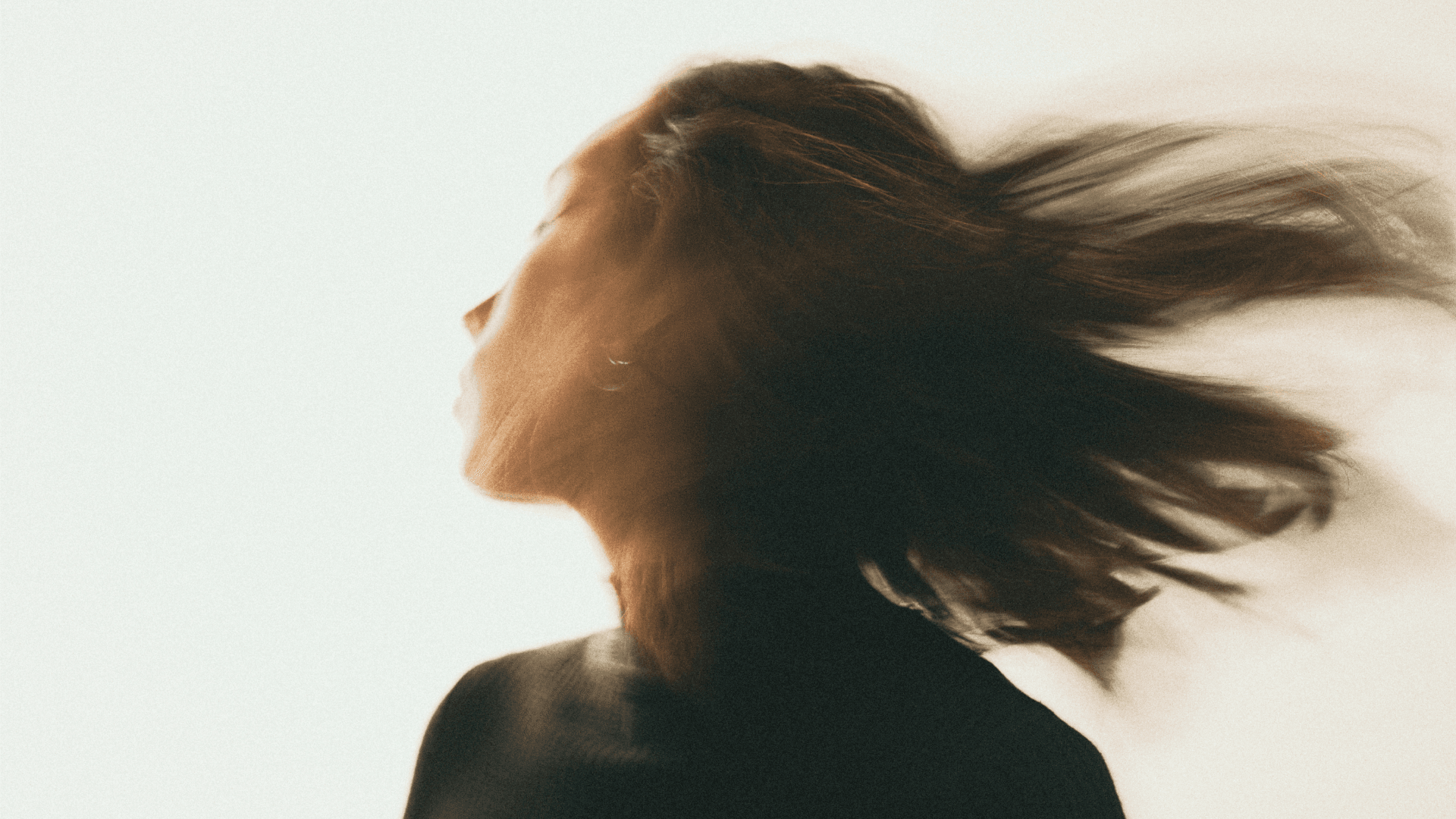 Blurred side profile of a person with long hair, captured mid-motion against a light background.