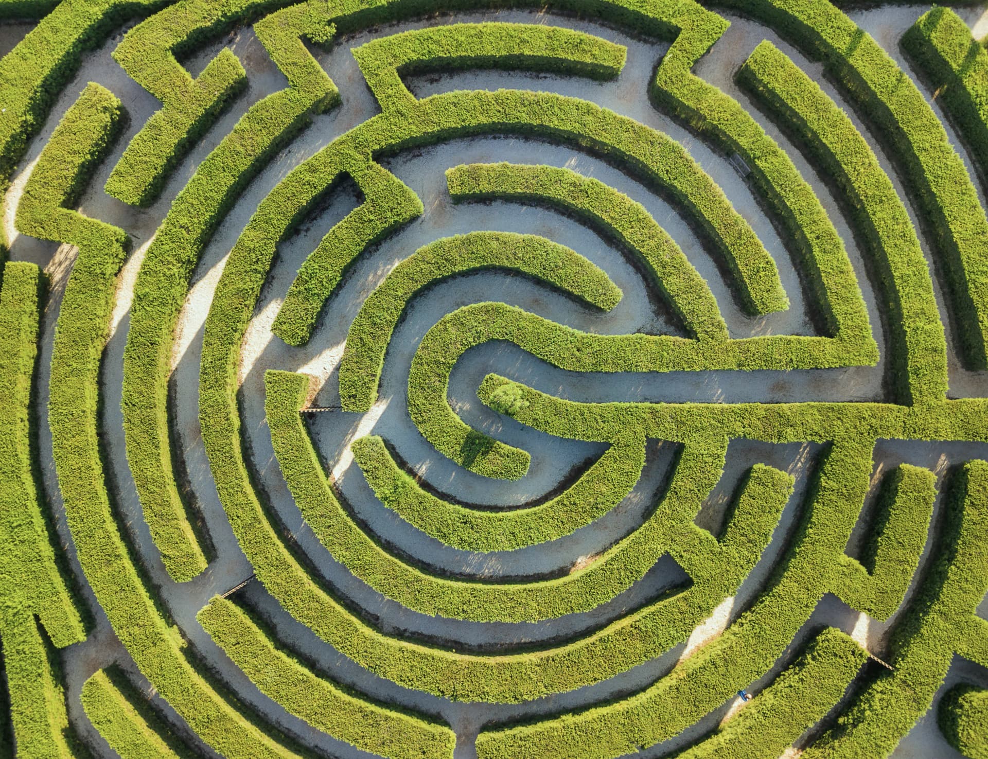 Aerial view of a circular hedge maze with intricate pathways of bright green hedges and sandy paths.