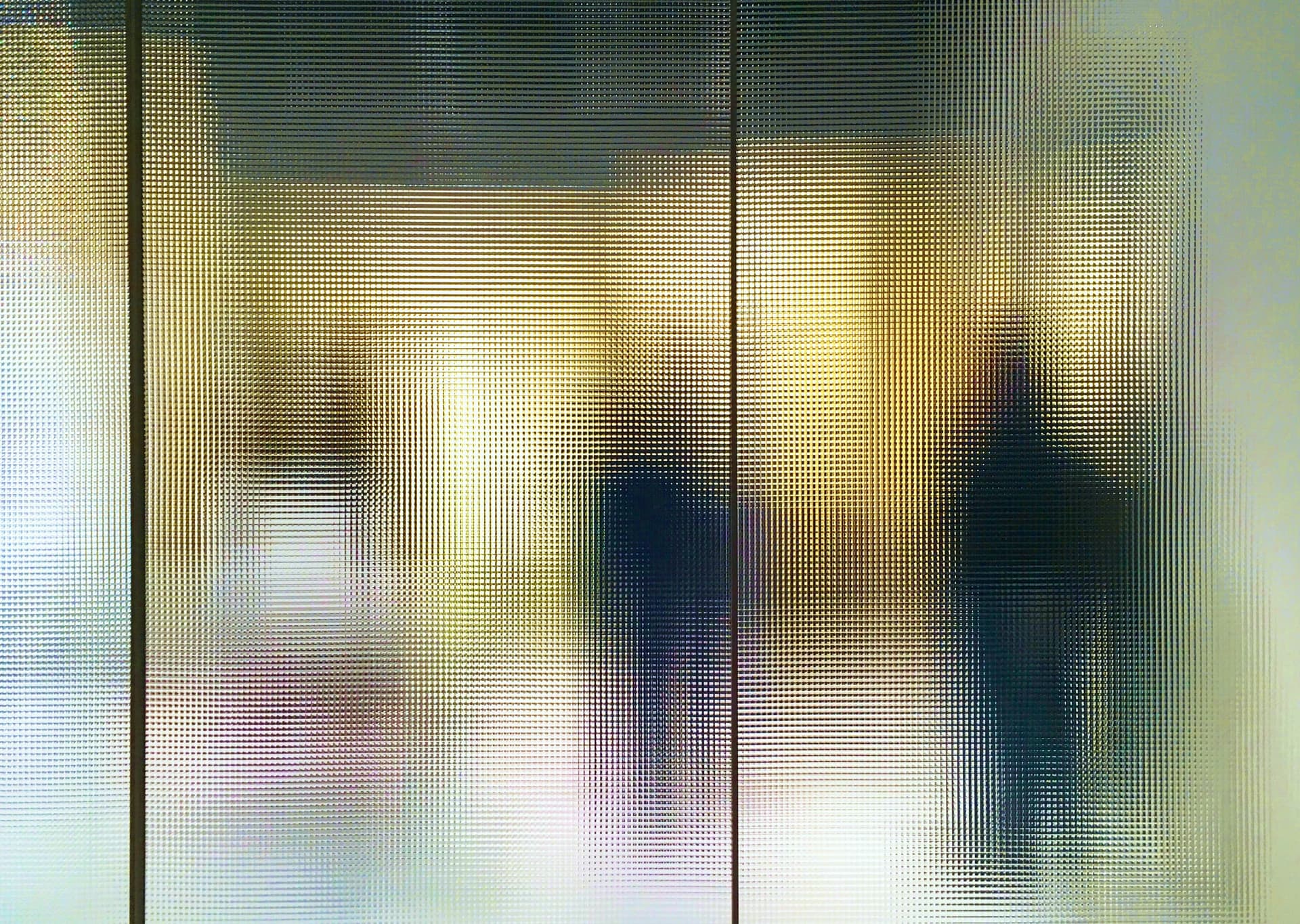 Blurry silhouettes of two people behind a textured glass wall, with warm lighting creating a soft, abstract visual effect.