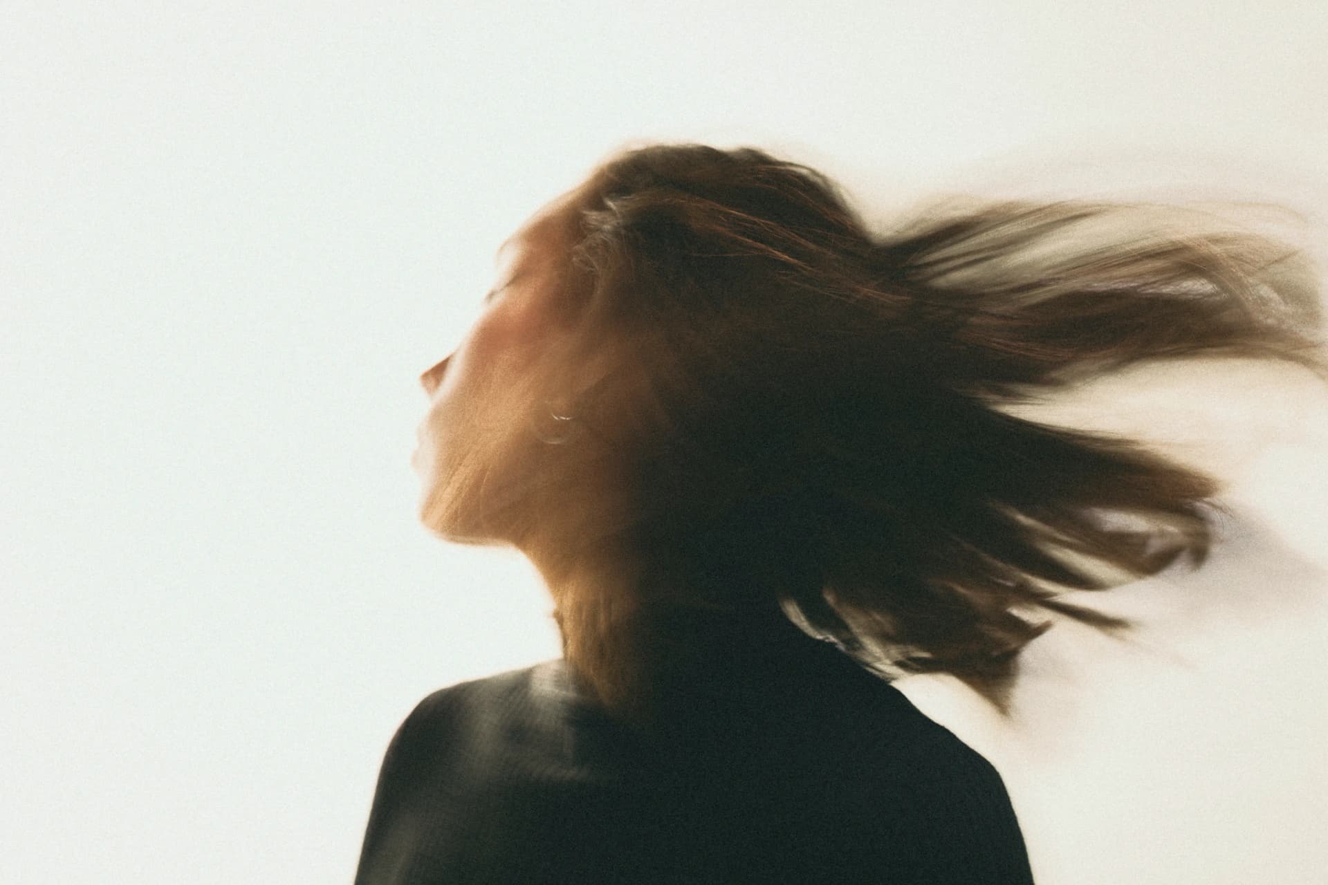 Profile of a person in motion, hair blurred as it sways, against a light background, suggesting dynamic movement.