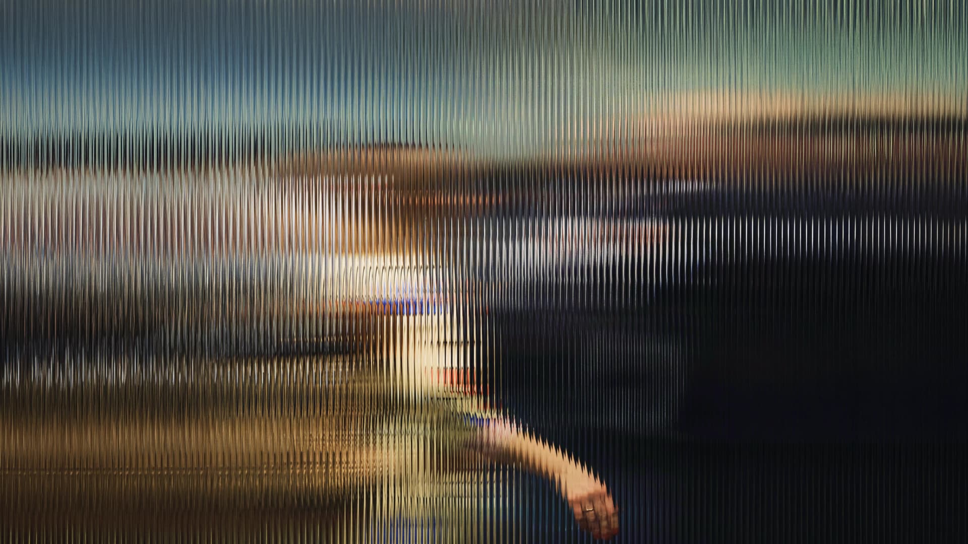 Blurry silhouette of a person behind a textured glass surface, creating a distorted and abstract visual effect.