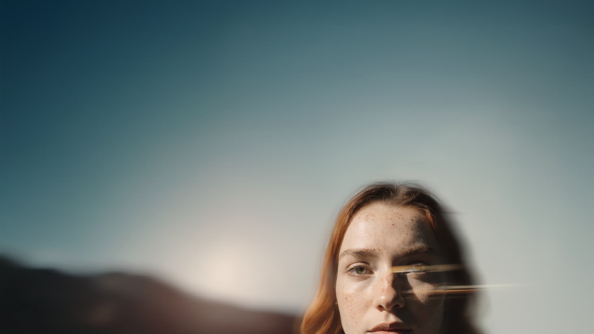 A woman partially visible against a bright blue sky with sunlight reflecting on the camera lens.