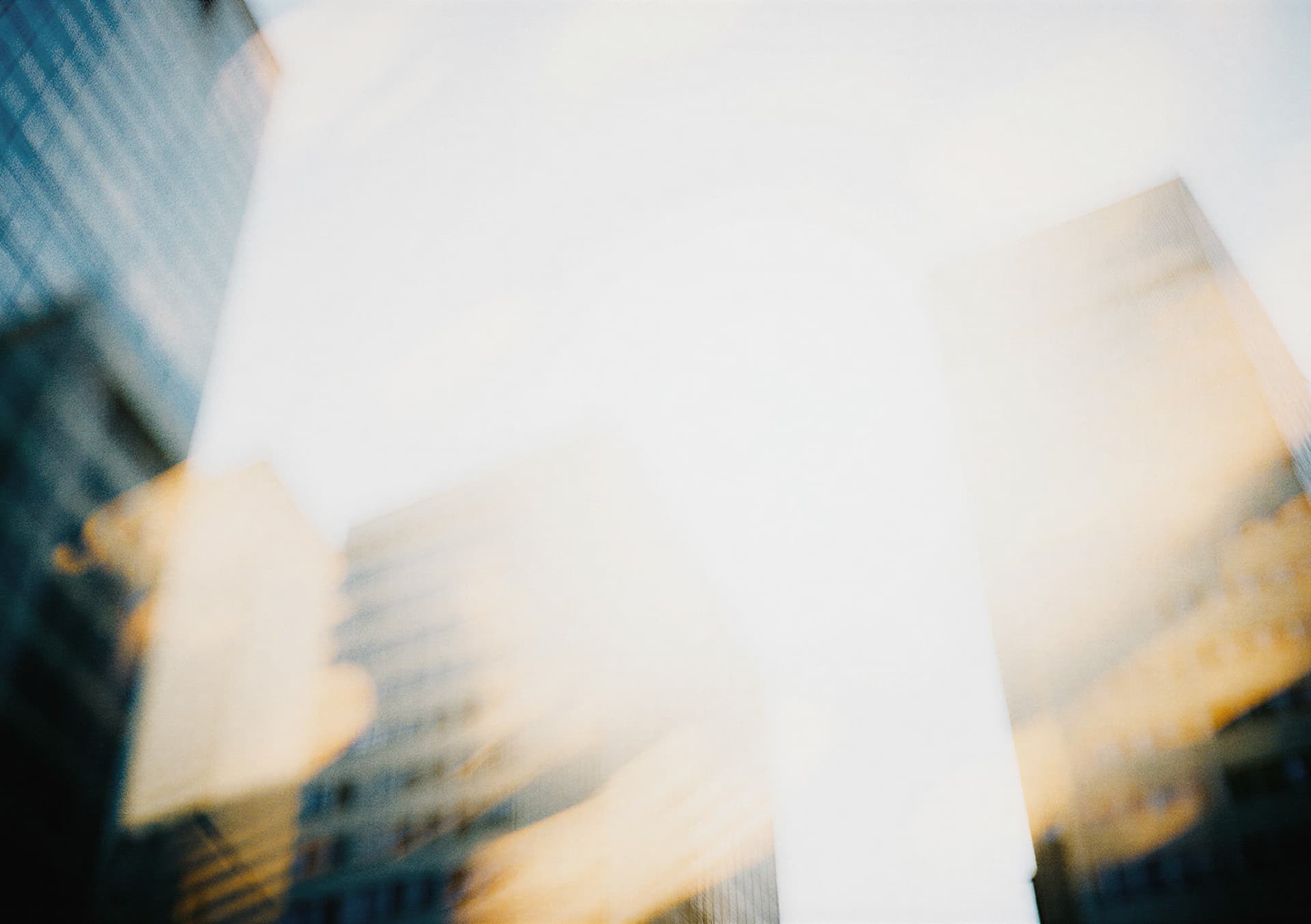 Abstract image of skyscrapers with a soft, blurry effect, blending blue and orange hues under a bright sky.