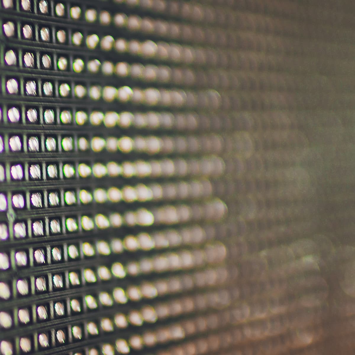 Close-up of a grid-like pattern with small, illuminated squares, creating a blurred effect with a gradient of colors.